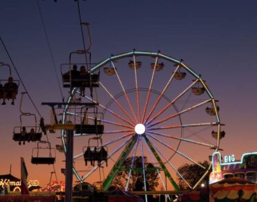 Evening sky with a lit Ferris wheel and chairlift ride at a fairground