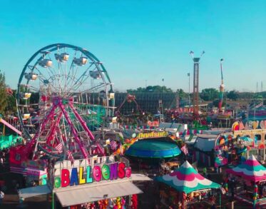 Aerial view of a bustling fair with a Ferris wheel, games, and colorful tents