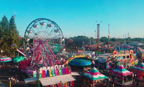 Aerial view of a bustling fair with a Ferris wheel, games, and colorful tents