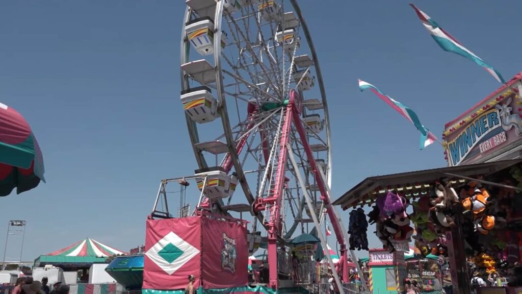A Ferris wheel and colorful carnival booths under a bright blue sky