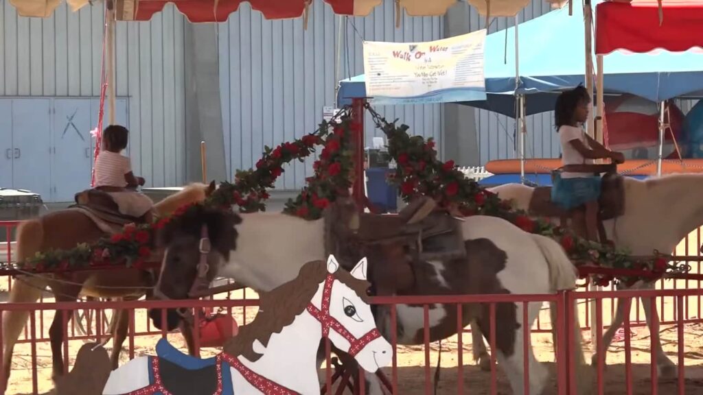 Children riding ponies on a carousel at a sunny fairground