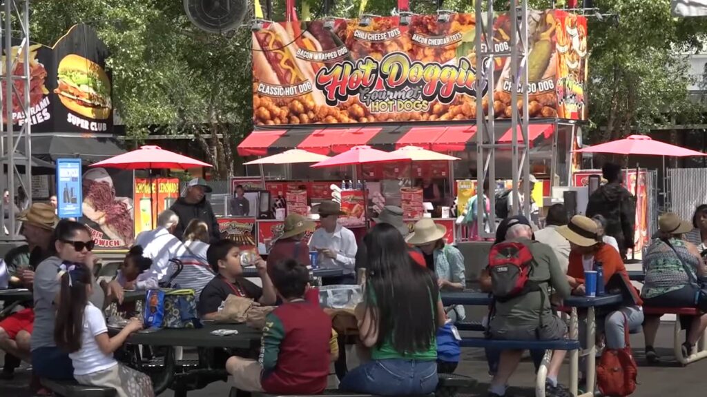 People enjoying food at picnic tables in a lively outdoor fair setting